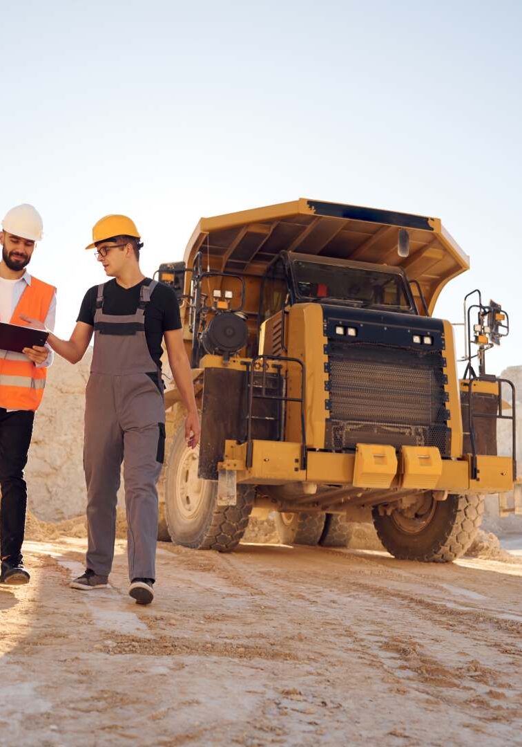 Standing near haul truck and talking about document. Two men in uniform are working together in the quarry.